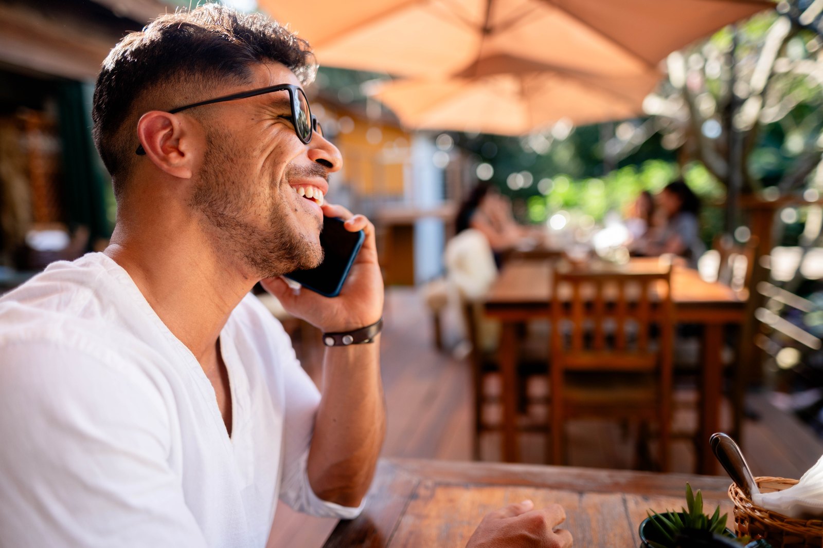 A man smiling while talking on his phone at a cafe