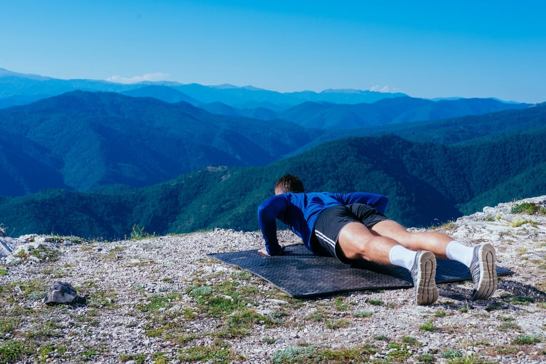 A man doing push-ups on a mountain top above the valley
