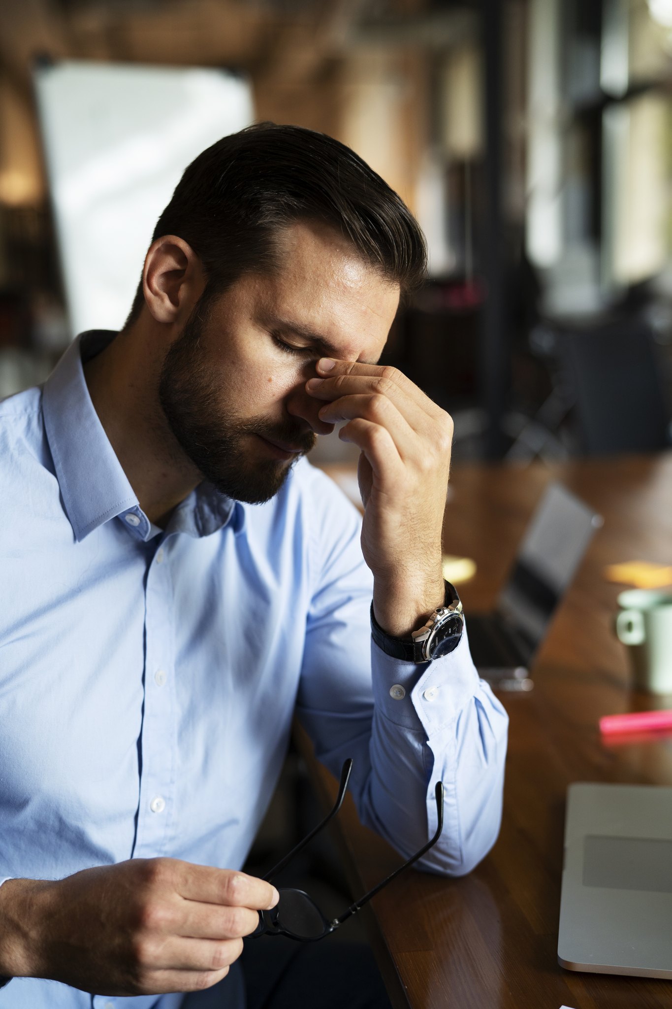 A tired man pinching the bridge of his nose at his desk
