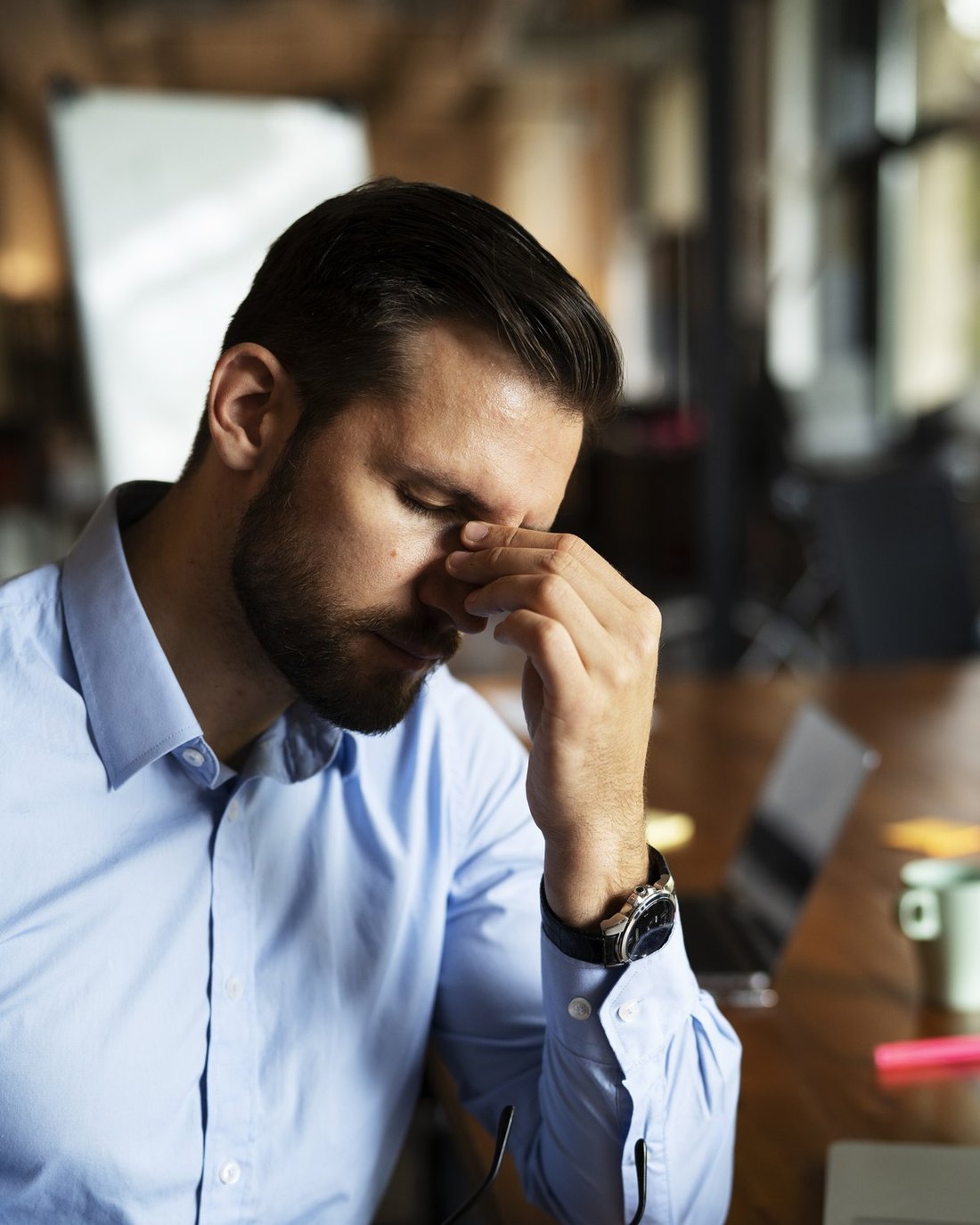 A tired man pinching the bridge of his nose at his desk